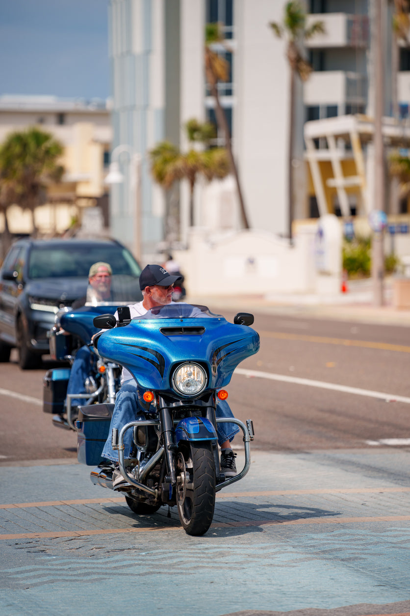 man riding a blue motorcycle down a palm tree lined street